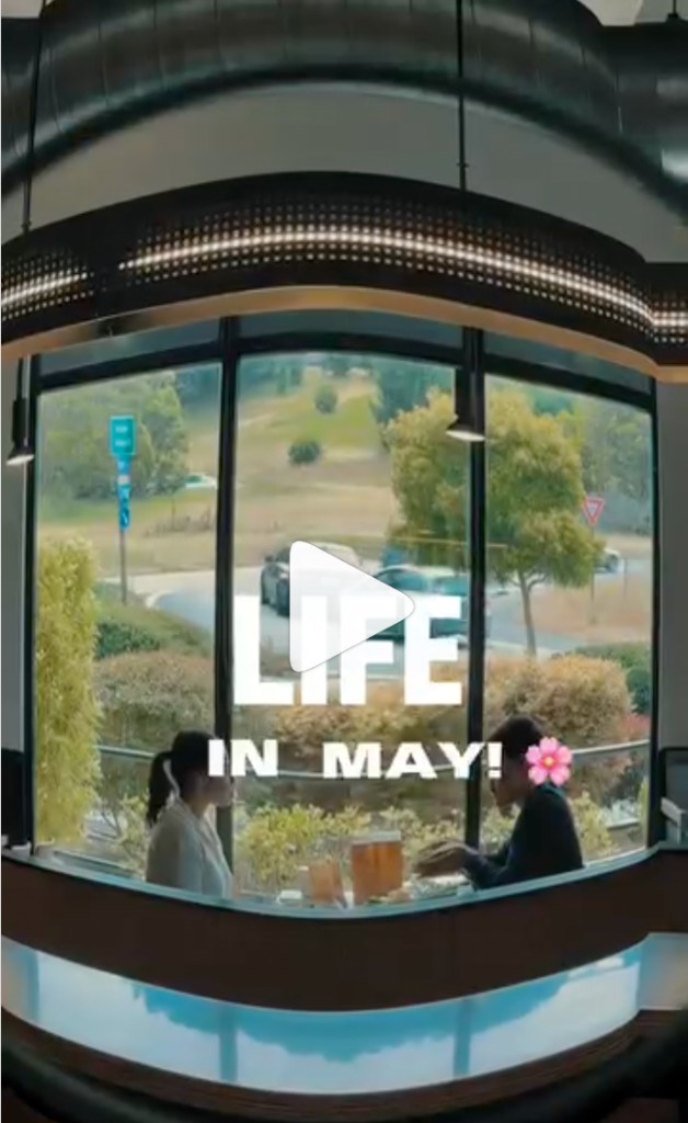Reel still: LIFE IN MAY with cherry blossom text, two people at a table by a curved window looking out to a street